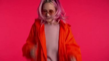 Pembe saçlı ve olağanüstü görünüşlü bir kız zaferin evet jestini gösteriyor. Sonuç elde etti, hedeflerine ulaştı. Kırmızı arka planda heyecanlı, mutlu bir hipster.