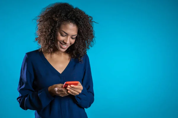 Mavi stüdyo duvarında akıllı telefondan karışık ırk görünümlü bir kız oyun oynuyor. Modern teknolojiyi kullanarak - uygulamalar, sosyal ağlar — Stok fotoğraf