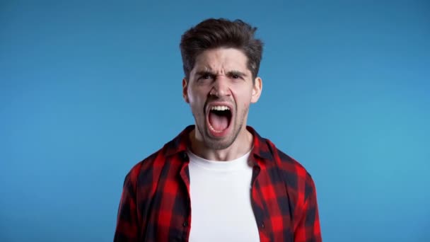 Young european stressed man in red shirt shouting isolated over blue background — Stock Video