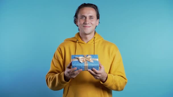 Jóképű férfi kezében karácsonyi vagy születésnapi ajándék doboz kék stúdió háttér — Stock videók