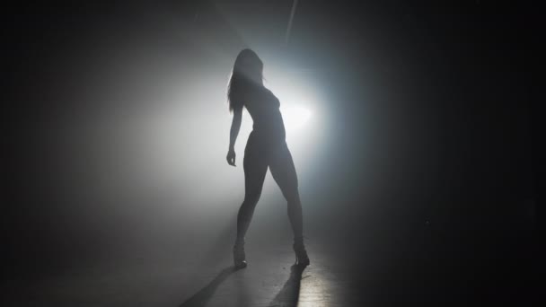Λεπτή σέξι σιλουέτα της γυναίκας που χορεύει σε σκουρόχρωμη σκηνή μπροστά στον προβολέα — Αρχείο Βίντεο