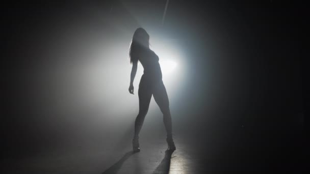 Slim silhouette sexy de femme dansant sur scène sombre fumée devant le projecteur — Video