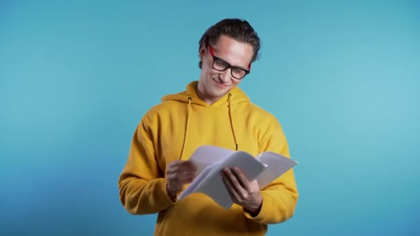 Junger gutaussehender Mann prüft Dokumente, Rechnungen, Berichte. Student isoliert auf blauem Grund — Stockvideo