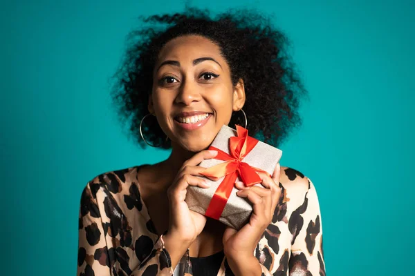 Piękna Afroamerykanka otrzymała pudełko z łukiem. Jest szczęśliwa i pochlebia jej uwaga. Dziewczyna na tle studia. — Zdjęcie stockowe