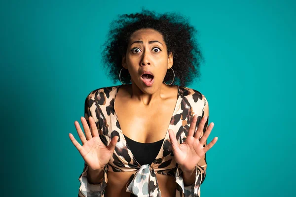 Mulher afro-americana assustada com cabelo encaracolado em camisa de leopardo com medo de algo e olha para a câmera com grandes olhos cheios de horror sobre fundo de parede azul . — Fotografia de Stock