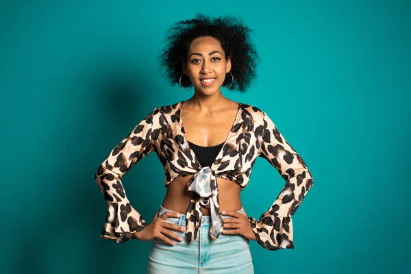 青い壁の背景にカメラに笑みを浮かべてヒョウの上にアフロの髪を持つかなりアフリカの女性。かわいい混合レースの女の子の肖像画. — ストック写真