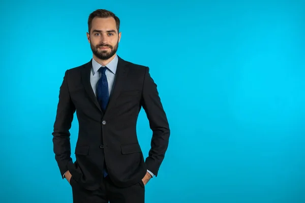 Espaço para cópia. Retrato de jovem empresário confiante de sucesso com barba isolada em fundo de estúdio azul. Homem de fato de negócios a olhar para a câmara e a sorrir. Retrato de cara bonito . — Fotografia de Stock