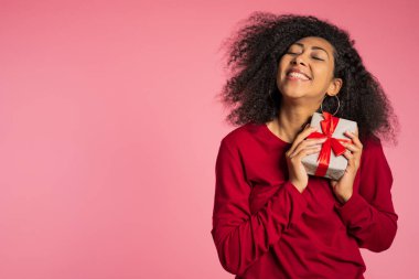Güzel Afrikalı Amerikalı kadın, üzerinde yay olan bir hediye kutusu aldı. O mutlu ve ilgiyle pohpohlanıyor. Stüdyo geçmişi olan kız.