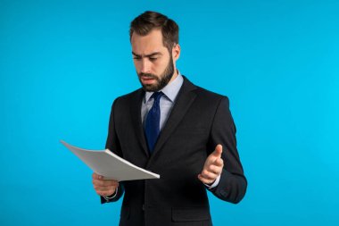 Ciddi işadamı patronu mavi arka plandaki stüdyoda izole edilmiş. İnsan çalışmaktan memnun değil. Takım elbiseli, belgeli, raporlu ya da sözleşmeli genç bir ofis çalışanı.