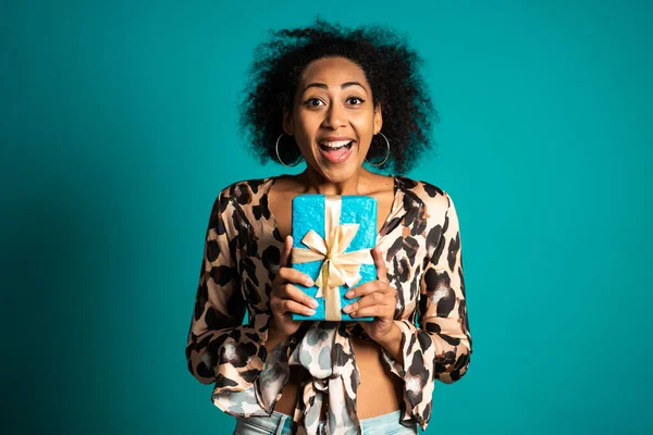 Bela mulher afro-americana recebeu caixa de presente com arco. Ela está feliz e lisonjeada pela atenção. Menina no fundo do estúdio . — Fotografia de Stock