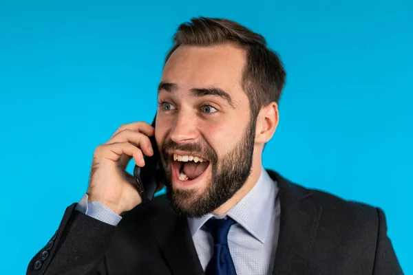 Überrascht aufgeregten fröhlichen Geschäftsmann, der auf Handy auf blauem Hintergrund spricht. Mann sagt wow. — Stockfoto