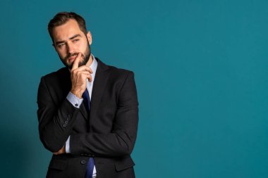 Ciddi düşünen bir iş adamı mavi arka plana bakıyor. Kafası karışmış, düşünceli yüz ifadeleri. Takım elbiseli yakışıklı erkek model..