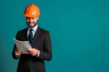 Takım elbiseli, miğferli, belgeli, inşaat projeli genç mühendis. Rapor ver. İşadamı, inşaatta olduğu gibi mavi arka planda da izole edilmiş. Boşluğu kopyala