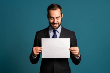 Beyaz yatay a4 kağıt poster tutan bir iş adamı. Uzayı kopyala Mavi arka planda kravatlı, takım elbiseli, gülümseyen yakışıklı adam..