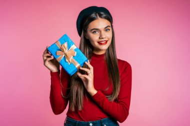 Heyecanlı kadın fiyonklu hediye kutusu aldı. O mutlu ve ilgiyle pohpohlanıyor. Pembe arka planı olan bir kız. Stüdyo çekimi