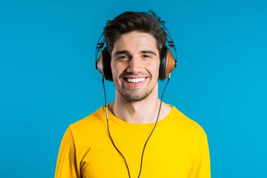 Mavi arka planda dans eden kulaklıklı yakışıklı bir adam. Parti, müzik, yaşam tarzı, radyo ve disko konsepti.