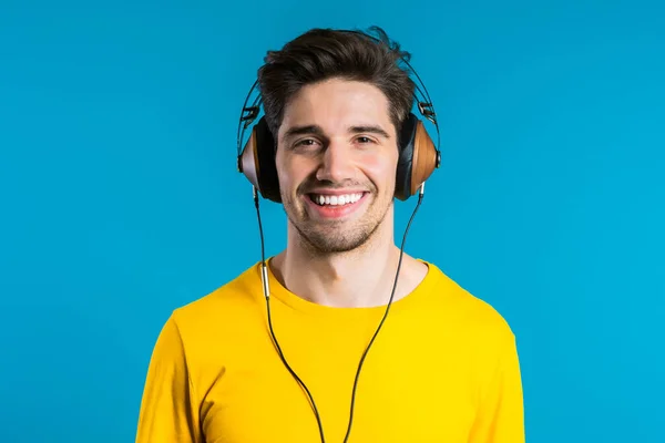 Un bel homme avec des écouteurs dansant isolés sur fond bleu. Fête, musique, style de vie, concept radio et discothèque . — Photo