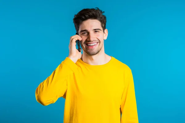 Jeune homme en couleurs vives usure parler sur téléphone portable sur fond bleu. Le mec branché a une conversation. Smartphone, concept technologique . — Photo