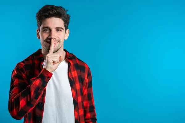 Homem bonito europeu segurando o dedo em seus lábios sobre fundo azul. Gesto de shhh, segredo, silêncio — Fotografia de Stock