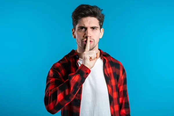 Homem bonito europeu segurando o dedo em seus lábios sobre fundo azul. Gesto de shhh, segredo, silêncio — Fotografia de Stock