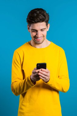 Adam mesajlaşırken akıllı telefondaki uygulamayı kullanıyor. Cep telefonuyla internette sörf yapan yakışıklı bir genç. Mavi stüdyo arka planı