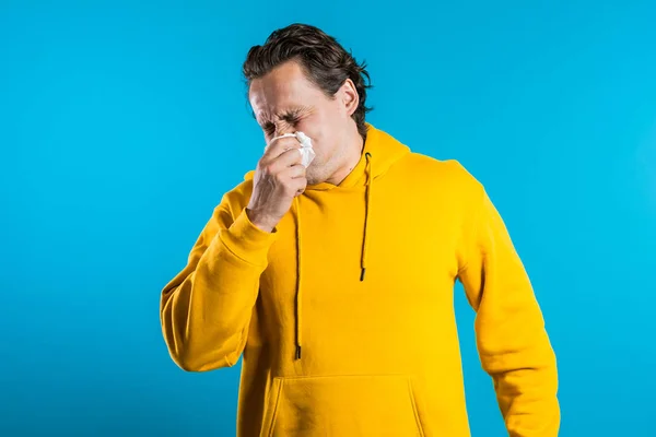 El joven estornuda en el tejido. El tipo aislado está enfermo, tiene un resfriado o una reacción alérgica. Salud, medicina, enfermedad, concepto de tratamiento — Foto de Stock