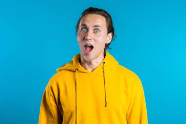 Mutlu Avrupalı adam şaşkınlıkla seviniyor. Şık saçlı yakışıklı adam mavi arka planda kameraya şaşırdı..