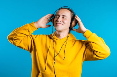 Mavi arka planda dans eden kulaklıklı yakışıklı bir adam. Parti, müzik, yaşam tarzı, radyo ve disko konsepti.