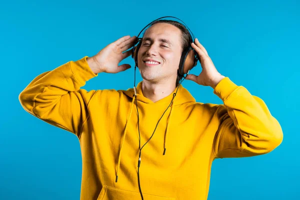 一个英俊的男人带着耳机，与蓝色背景隔离跳舞。 派对、音乐、生活方式、收音机和迪斯科音乐概念. — 图库照片