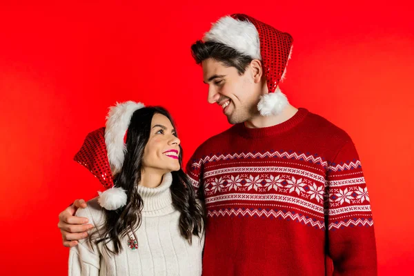 Kırmızı stüdyo arka planında Noel süsleri takmış genç bir çiftin portresi. Aşk, tatiller, mutluluk konsepti.