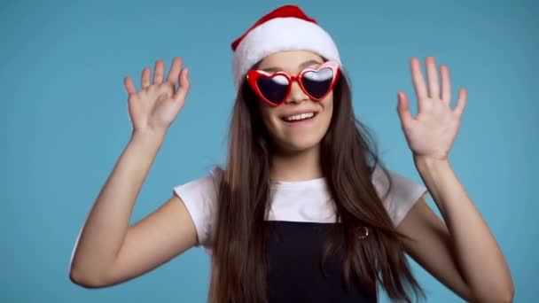 Dansen meisje met Santa hoed hebben plezier, vreugde geïsoleerd over blauwe studio achtergrond. Concept van Kerstmis, Nieuwjaar, geluk, feest, winnen. — Stockvideo