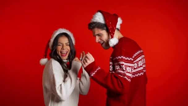 Beau jeune couple en chapeaux de Père Noël danser, s'amuser, se réjouit sur studio rouge. Concept de Noël, Nouvel An, bonheur, fête, gagner . — Video