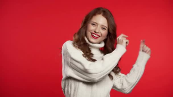Baile divertido en el estudio. Retrato de mujer joven atractiva en suéter blanco bailando sobre fondo rojo. 4k — Vídeo de stock