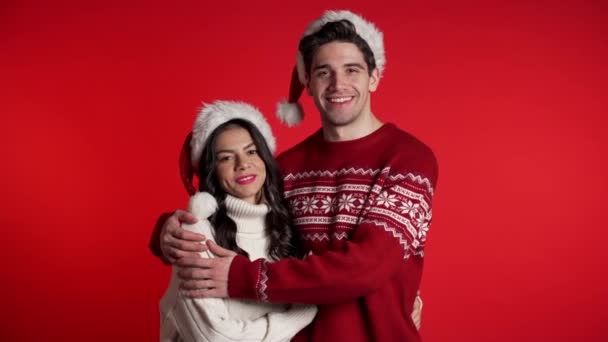Retrato de jovem casal em decorações de Natal Papai Noel chapéus sobre fundo estúdio vermelho. Amor, férias, conceito de felicidade . — Vídeo de Stock