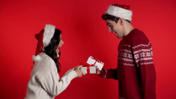 Casal jovem no Natal Papai Noel troca presentes no fundo do estúdio vermelho. Amor, férias, conceito de felicidade . — Vídeo de Stock