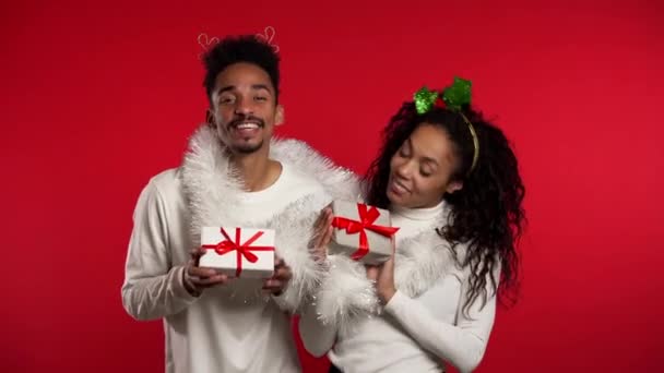 Young african american couple with christmas gift box dancing isolated on red background studio. New 2020 year decorations, presents, party, happiness concept. — ストック動画