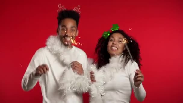 Jovem casal afro-americano com faíscas de fogo de Natal bengala isolado no estúdio de fundo vermelho. Nova 2020 ano decorações, festa, conceito de felicidade . — Vídeo de Stock