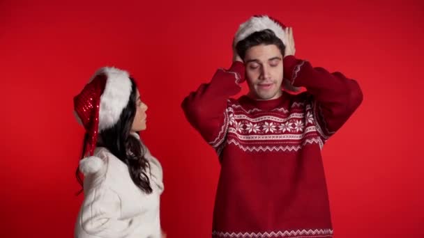 Noel şapkalı genç bir kadın stüdyoda kırmızı arka planda kocasına ya da erkek arkadaşına duygusal olarak bağırıyor. Sıkılmış adam kulaklarını elleriyle kapatır. Çatışma kavramı, ilişkilerdeki sorunlar. — Stok video