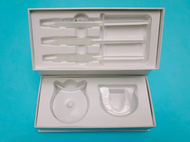 Mavi arka planda izole edilmiş kutuyla beyazlatma seti. Ev beyazlatma jeli tepsisi opalezi. Diş bakımı için modaya uygun bir alet. İlaç, diş güzellik malzemeleri.