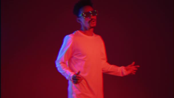 Young african american man in white wear smiling and dancing in good mood on red background with neon light. Slow motion. — Stock Video