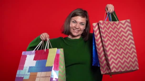 Mujer joven feliz con bolsas de papel de colores después de comprar aislado en el fondo del estudio rojo. Venta estacional, compras, gasto en concepto de regalos — Vídeos de Stock
