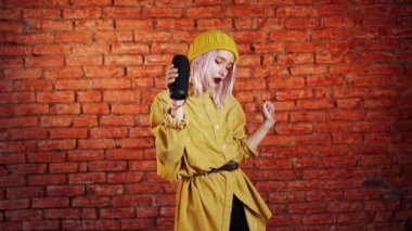 Pembe saçlı, eğlenen, gülümseyen, stüdyoda kablosuz taşınabilir hoparlörle dans eden alışılmadık bir kadın. Müzik, dans konsepti, ağır çekim