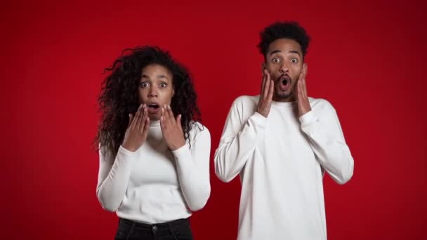 Verbazingwekkende Afro-Amerikaanse man en vrouw geschokt, zeggend Wow. jong paar in wit verrast naar camera over rode achtergrond. — Stockvideo