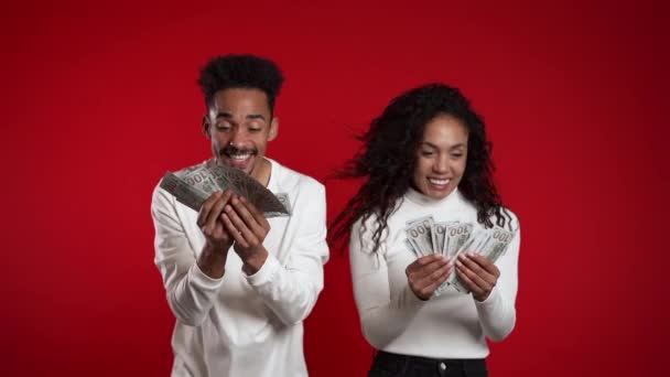 Задоволена щаслива подружня пара африканців, що показує гроші - банкноти США на червоній стіні. Символ успіху, перемоги, перемоги. Повільний рух — стокове відео