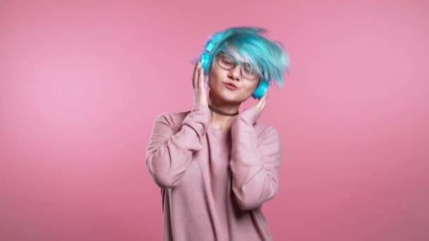 Ungewöhnliche Frau mit blauen Haaren, die Spaß hat, lächelt, mit Kopfhörern im Studio vor rosa Hintergrund tanzt. Musik, Tanzkonzept, Zeitlupe — Stockvideo