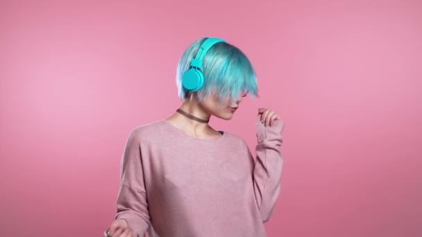 Unusual woman with blue hair having fun, smiling, dancing with headphones in studio against pink background. Music, dance concept, slow motion — Stock Video