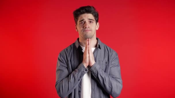 Knappe man in hemd biddend over rode achtergrond. Europees ras guy smeken iemand. — Stockvideo