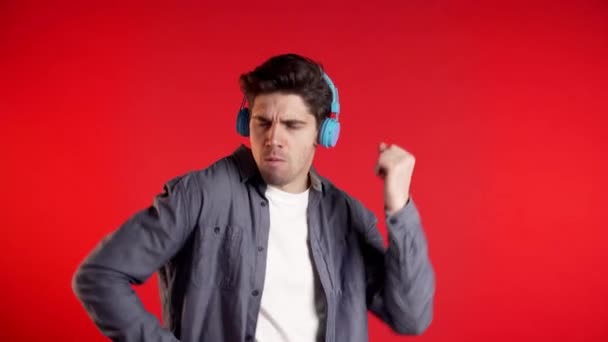 Hombre guapo con auriculares bailando aislado sobre fondo rojo. Fiesta, música, estilo de vida, radio y disco concepto . — Vídeos de Stock