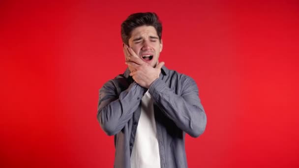 Joven hombre guapo en camisa de mezclilla con dolor de dientes en el fondo rojo del estudio. Dolor de muelas, problemas dentales, estomatología y concepto de medicina . — Vídeo de stock