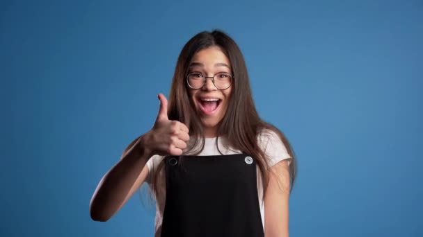 Joven mujer asiática con maquillaje perfecto haciendo pulgares hacia arriba signo sobre fondo azul. Ganador. Éxito. Chica positiva sonríe a la cámara. Lenguaje corporal . — Vídeos de Stock